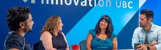 two women and two men chatting in front of a blue wall with the Innovation UBC wordmark on it.