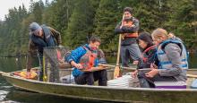 Three males and two females in a small metal fishing boat surrounded by fishing gear and research equipment